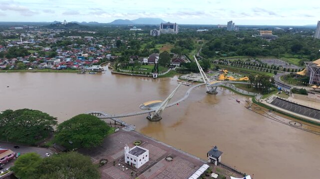 Aerial view of the sarawak state legislative assembly building with golden dome roof and modern pedestrian darul hana bridge crossing the sarawak river
