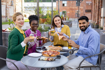 Diverse group of friends enjoying pizza and drinks together outdoors at a restaurant.