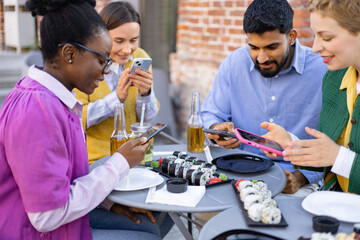 Friends gather for a sushi meal, each engrossed in their phones, creating a blend of social connection and digital engagement.