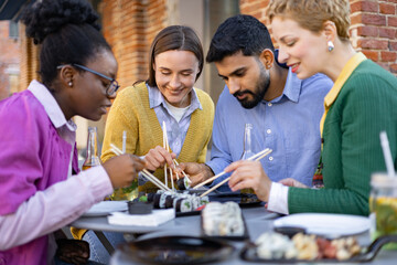 Friends enjoying sushi and drinks together at an outdoor restaurant, focusing on food and socializing.
