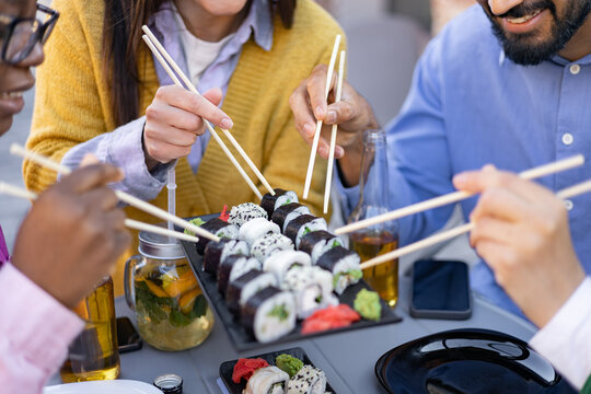 A group of friends enjoys a delicious sushi meal outdoors, using chopsticks to savor various sushi rolls. - Powered by Adobe