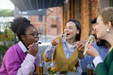 Diverse group of friends enjoying sushi outdoors, laughing and having a good time during a casual...