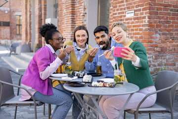 A diverse group of friends enjoys sushi and takes a selfie at an outdoor cafe.