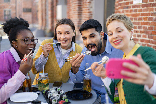 Friends enjoy sushi together, taking a selfie outdoors. They are smiling and having fun.