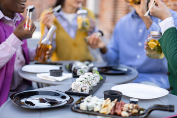 Friends enjoying sushi outdoors, sharing food and drinks at a cafe or restaurant.
