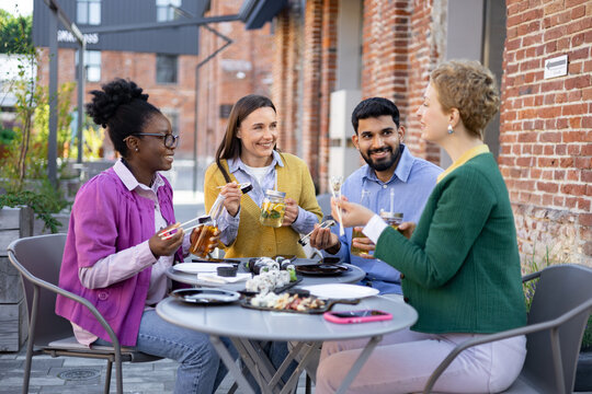 Four diverse friends enjoy a sushi lunch outdoors, laughing and chatting at a restaurant.