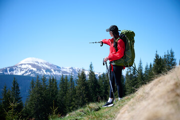 Female hiker with backpack and trekking poles walking in the mountains. Adventure lifestyle in...