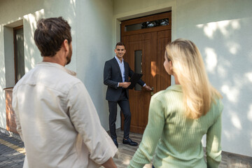 Real estate agent opening door for couple at modern house tour