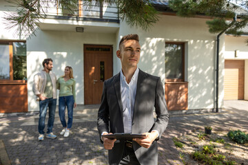 Real estate agent with clipboard outside modern house with couple