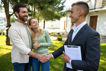 Pair celebrating home purchase with agent in green yard area