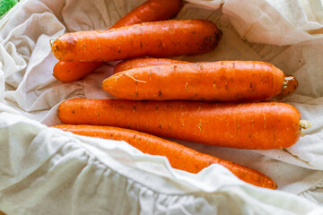 Fresh carrots neatly arranged in a wooden crate lined with off-white cloth. The vibrant orange color of the carrots pops against the neutral background, creating a vivid and appetizing composition