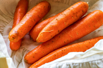 Fresh carrots neatly arranged in a wooden crate lined with off-white cloth. The vibrant orange color of the carrots pops against the neutral background, creating a vivid and appetizing composition