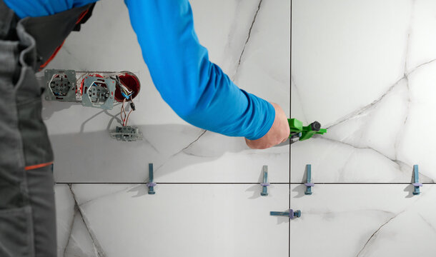 Man installing ceramic granite tiles on the wall in the new apartment. Plumber installing ceramic tile in customers bathroom, getting ready to sell home. Tile leveling system.