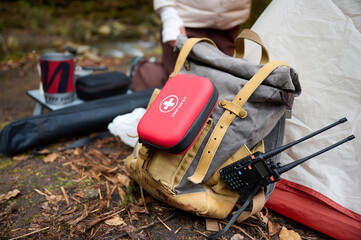 Red first aid kit on a backpack near a camping tent. Injuries and damage in the forest. Concept of medical support on a walk. Emergency assistance in case of injury on the trip a set of medicine