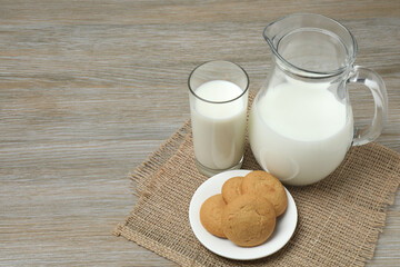 glass and jug with milk, cookies on wooden background