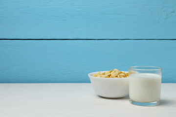 glass with milk, cornflakes on white wooden background