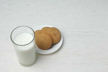 glass with milk and cookies on white wooden background