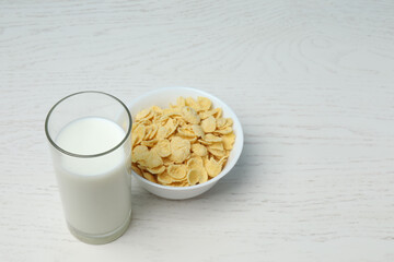 glass with milk, cornflakes on white wooden background