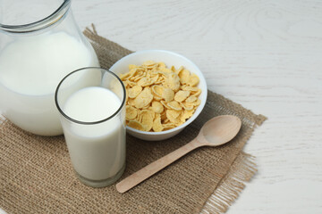 glass and jug with milk, cornflakes on white wooden background
