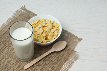 glass with milk, cornflakes on white wooden background