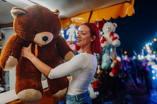 Happy young woman holding a giant teddy bear at the funfair