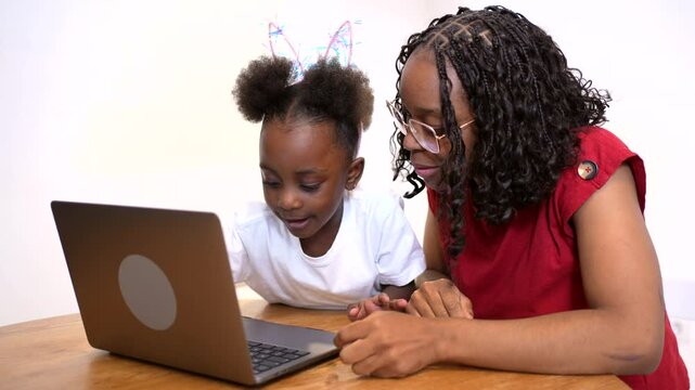 Concentrated mother helping her little daughter to use a laptop at home, isolated over white background