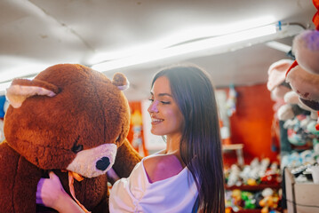 Happy young woman holding a giant teddy bear at amusement park