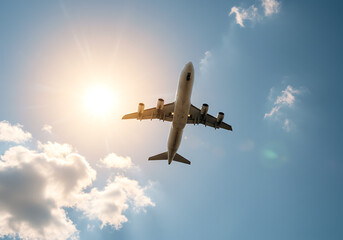 commercial airplane flying in clear blue sky with bright sun flare