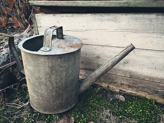 Rustic metal watering can beside weathered wooden plank.