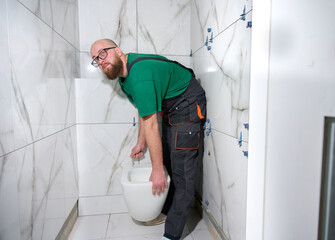 Plumber installing toilet. Modern toilet installation. Worker installing a wall-hung toilet on the...