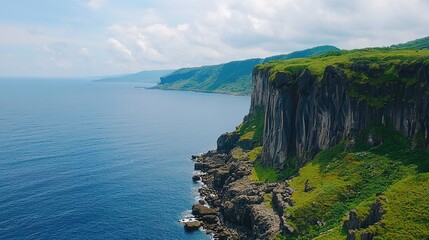 Dramatic coastal cliffs covered in greenery overlook a deep blue ocean under a partly cloudy sky.