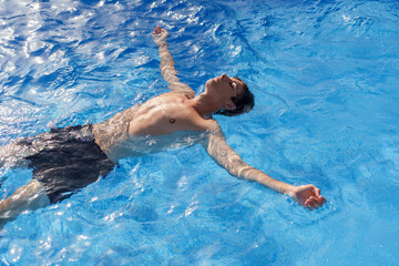 Relaxed male drifting in bright blue pool water, enjoying sunny day with carefree summer leisure...