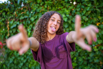 Curly haired woman playfully sticking tongue out, pointing fingers while radiating youthful,...
