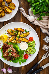 Grilled beef steak with baked potato wedges and fresh vegetables on wooden table	