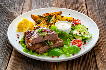 Grilled beef steak with baked potato wedges and fresh vegetables on wooden table	