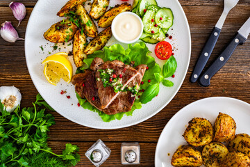 Grilled beef steak with baked potato wedges and fresh vegetables on wooden table	