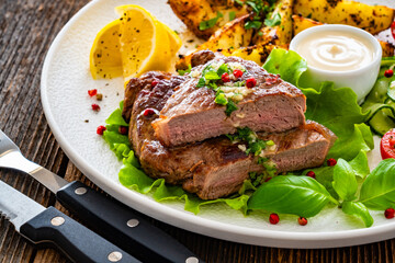 Grilled beef steak with baked potato wedges and fresh vegetables on wooden table	