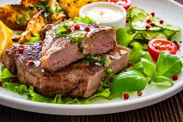 Grilled beef steak with baked potato wedges and fresh vegetables on wooden table	