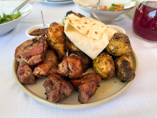 Close-up of a delicious and hearty meal. Juicy grilled pork and chicken, savory baked potatoes, and flatbread arranged on a ceramic plate with sauce and salad in a restaurant setting