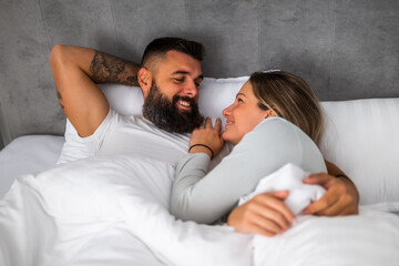 Young happy loving couple is lying in bed in the morning. They are relaxing and enjoying.
