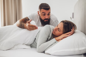 Couple is lying in bed and arguing. The woman is angry and offended and man is talking.