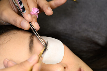 Detailed view of eyelash technician attaching lashes with tweezers