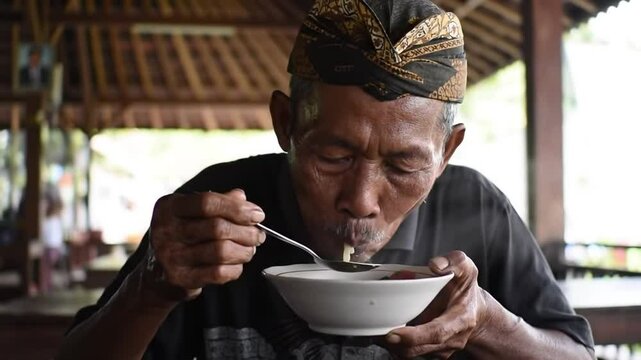 Elderly man enjoying a traditional meal in a rustic restaurant surrounded by lush greenery