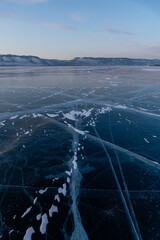 Expansive frozen lake surface with intricate ice patterns and snow patches under a clear blue sky,...