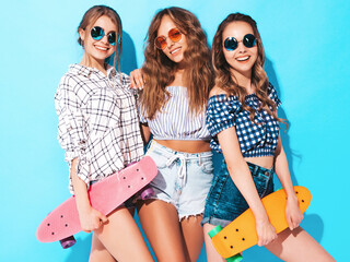 Three young stylish smiling beautiful female with penny skateboards. Women in summer hipster...