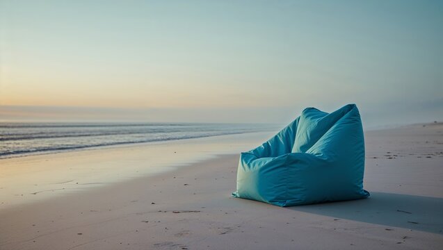 Empty blue bean bag chair sits alone on a tranquil beach during sunset with gentle waves lapping at the shore
