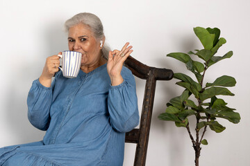 Portrait of an indian stylish look smiling mature elder 60s woman sitting relaxing with cup of tea,...