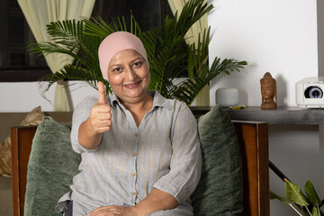 Recovering Cancer Patient Showing thumbs up at home. Indian female cancer patient sitting in living...