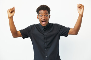 Fototapeta premium Excited young black man celebrating success with raised hands, conveying joy and enthusiasm in a bright and cheerful atmosphere. Perfect for inspirational themes.