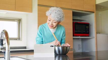 タブレットを見ながら料理するシニア女性